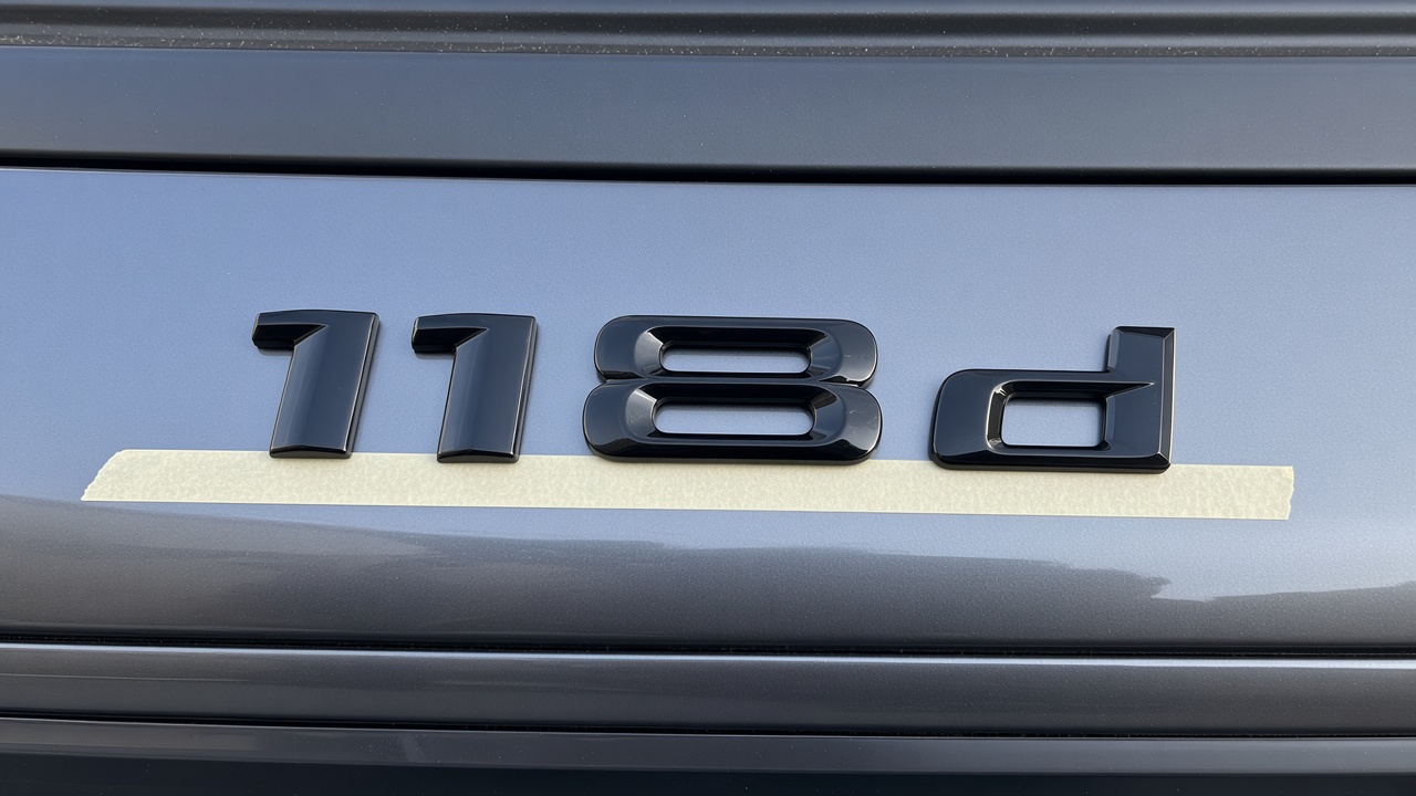 Gloss black 118d letters lined up on masking tape across a boot lid